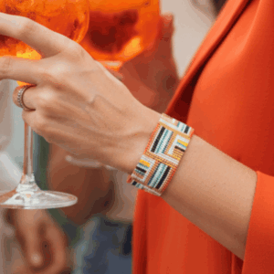 Bracciale di perline, realizzato a mano con perline in vetro indossato da donna con giacca arancione che sta bevendo un drink