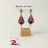 Orecchini pendenti forma a lanterna tridimensionale piena colore oro, nero, blu e rosso su uno sfondo chiaro con perline in vetro rosse