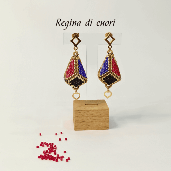Orecchini pendenti forma a lanterna tridimensionale piena colore oro, nero, blu e rosso su uno sfondo chiaro con perline in vetro rosse