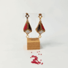 Orecchini pendenti forma a lanterna tridimensionale piena colore oro, nero, bianco e rosso su uno sfondo chiaro con perline in vetro rosse
