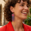 Orecchini di perline viola iridescenti a frangia con cuore rosso, indossato da donna sorridente con abito rosso, come sfondo la città