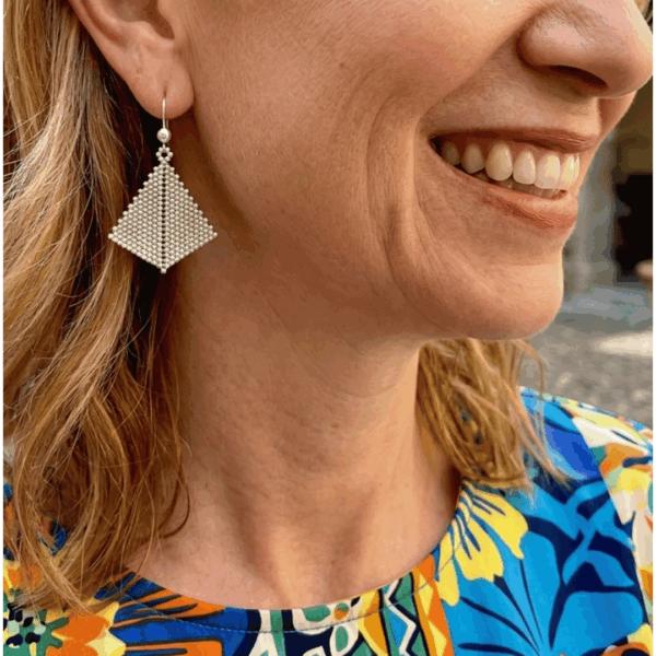 Orecchini pendenti di perline a forma di aquilone indossati da donna bionda con outfit colorato