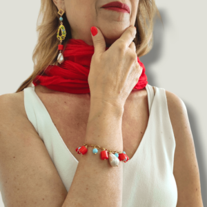 Donna con capelli biondi, foulard rosso e abito bianco indossa un bracciale charns di corallo, turchese e perla scaramazza e orecchini siciliani