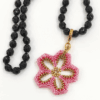 CCollana Fiore rosa realizzato a mano con perline in vetro e collana, con cristalli neri di Boemia nodi. Sfondo bianco.