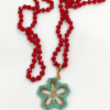 Collana Fiore turchese realizzato a mano con perline in vetro e collana, con cristalli rossi a nodi. Sfondo bianco.