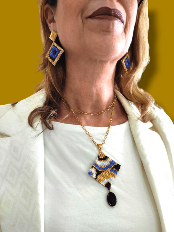 Su uno sfondo dorato dettaglio di donna che indossa una maglia bianca e una giacca bianca, una collana con ciondolo quadrato e orecchini grandi quadrati
