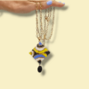 Sullo sfondo giallino una collana con catena in acciaio dorato e ciondolo dal design anni 60/70 colore nero, bianco, oro, pervinca e giallo