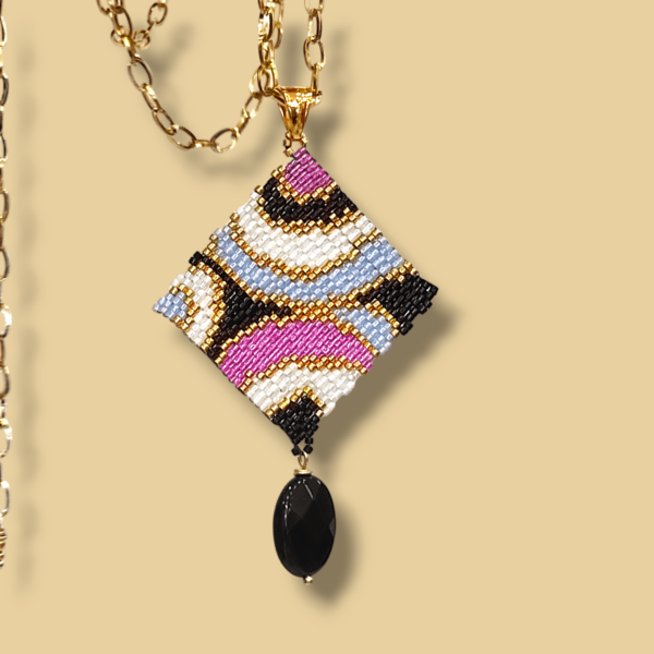 Sullo sfondo dorato una collana con catena in acciaio dorato e ciondolo dal design anni 60/70 colore nero, bianco, oro, azzurro e rosa