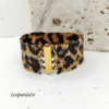 Inquadratura ravvicinata di un bracciale artigianale a fascia larga con motivo maculato leopardato, realizzato con perline Miyuki nere, oro e bronzo metallizzato. Al centro spicca la chiusura a baionetta in metallo dorato lucido.