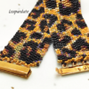Inquadratura ravvicinata di un bracciale artigianale a fascia larga con motivo maculato leopardato, realizzato con perline Miyuki nere, oro e bronzo metallizzato. Al centro spicca la chiusura a baionetta in metallo dorato lucido.