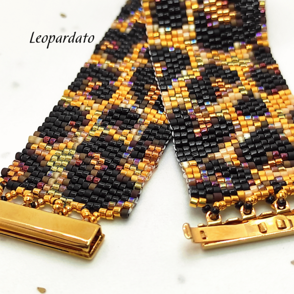 Inquadratura ravvicinata di un bracciale artigianale a fascia larga con motivo maculato leopardato, realizzato con perline Miyuki nere, oro e bronzo metallizzato. Al centro spicca la chiusura a baionetta in metallo dorato lucido.