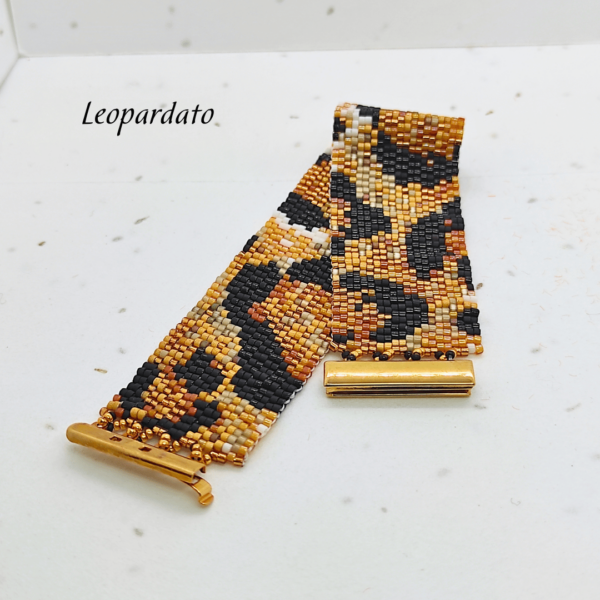 Bracciale rigido a fascia larga realizzato a mano con perline di vetro Miyuki con motivo leopardato animalier nei toni del nero, oro e marrone, dotato di chiusura a incastro in metallo dorato lucido su sfondo chiaro.