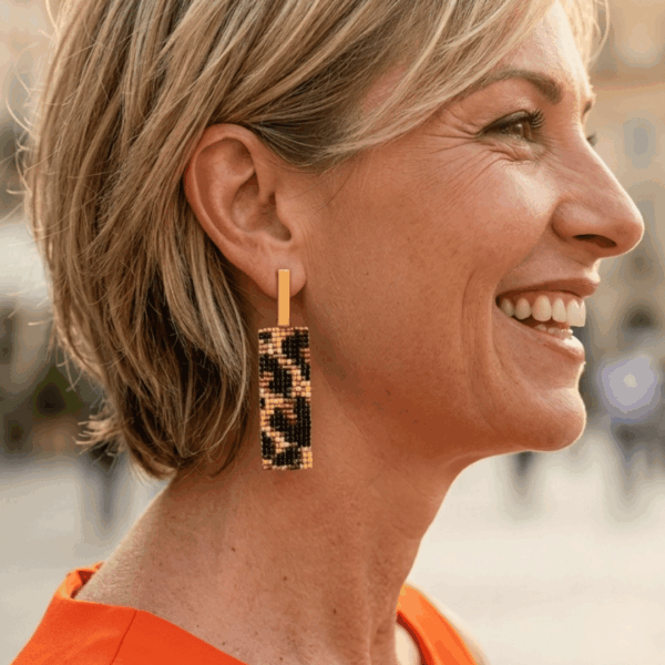 Orecchini pendenti in stile animalier ghepardato indossato da donna con i capelli biondi e outfit arancione