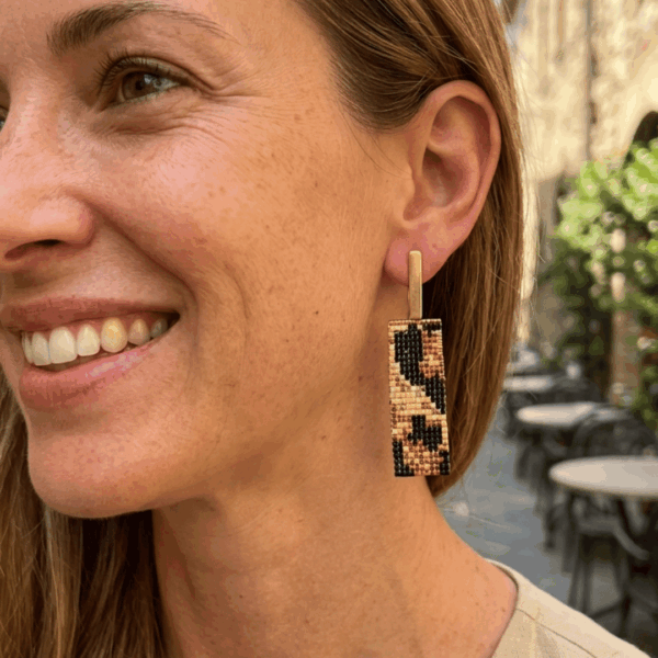 Orecchini pendenti in stile animalier leopardato indossato da donna con i capelli biondi e outfit beige