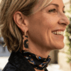 Orecchini pendenti in stile animalier indossato da donna con i capelli biondi e outfit nero