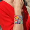 Bracciale a fascia alta di perline colorate design astratto con chiusura scorrevole in acciaio, indossato da donna con outfit rosso