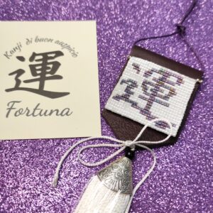 Amuleto Kanji della fortuna, realizzato con perline in vetro e nappa bianca pendente, su sfondo viola