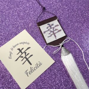 Amuleto Kanji della felicità, realizzato con perline in vetro e nappa bianca pendente, su sfondo viola
