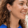 Orecchini a lobo di perline con catena pendente centrale, indossata da donna con outfit blu e capelli scuri ricci.