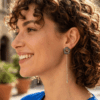 Orecchini a lobo di perline con catena pendente centrale, indossata da donna con outfit blu e capelli scuri ricci.