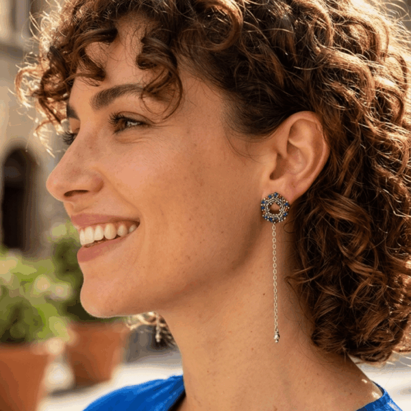 Orecchini a lobo di perline con catena pendente centrale, indossata da donna con outfit blu e capelli scuri ricci.