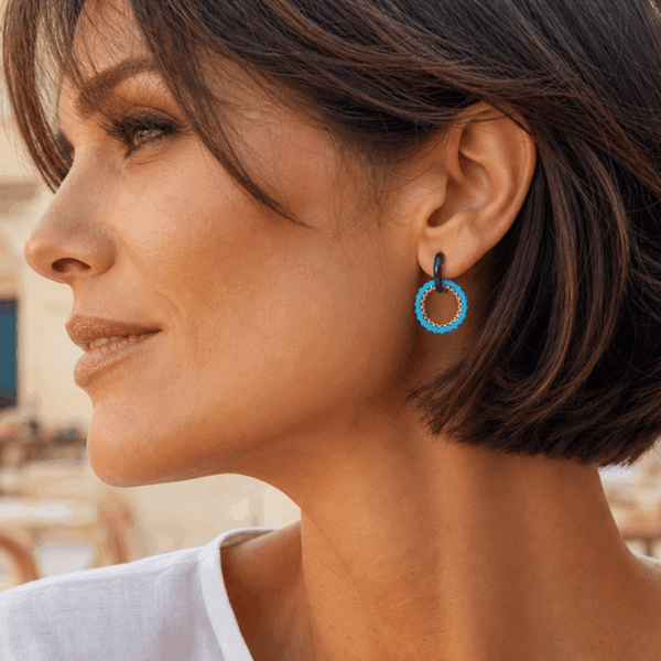 Orecchini a cerchio in acciaio dorato e resina,e cerchio di perline azzurro, indossato da donna con capelli corti e maglietta bianca