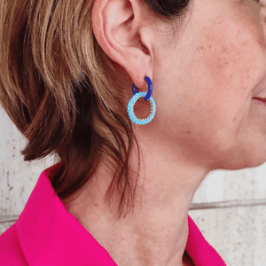 Orecchini a cerchio in acciaio dorato e resina,e cerchio di perline azzurro, indossato da donna con giacca fucsia