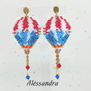 Orecchini pendenti a forma di mongolfiera firmati Vanitage Gioielli, realizzati a mano con perline di vetro nei toni del rosso, bianco, azzurro e blu, completati da catenella dorata e cristalli pendenti.
