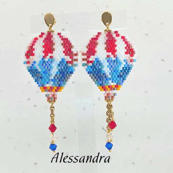 Orecchini pendenti a forma di mongolfiera firmati Vanitage Gioielli, realizzati a mano con perline di vetro nei toni del rosso, bianco, azzurro e blu, completati da catenella dorata e cristalli pendenti.