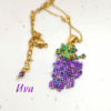 Collana con ciondolo a forma di grappolo d'uva viola e foglie verdi realizzato a mano con micro perline di vetro tessute, abbinata a catenina sottile dorata.
