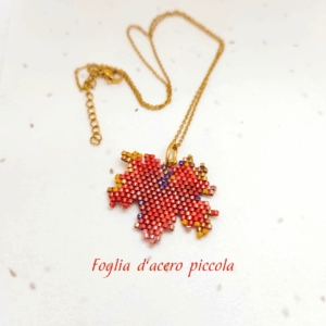 Collana con ciondolo a forma di piccola foglia d'acero rossa e arancione, realizzata con un mosaico di perline di vetro tessuto a mano e abbinata a una catenina dorata.