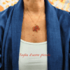 Collana con ciondolo a forma di piccola foglia d'acero rossa e arancione, realizzata con un mosaico di perline di vetro tessuto a mano e abbinata a una catenina dorata. Indossato