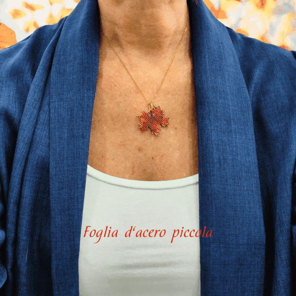 Collana con ciondolo a forma di piccola foglia d'acero rossa e arancione, realizzata con un mosaico di perline di vetro tessuto a mano e abbinata a una catenina dorata. Indossato