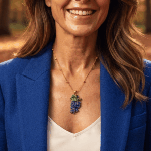 Collana con ciondolo a forma di grappolo d'uva viola e foglie verdi realizzato a mano con micro perline di vetro tessute, abbinata a catenina sottile dorata, indossata da donna con giacca blu