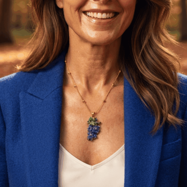 Collana con ciondolo a forma di grappolo d'uva viola e foglie verdi realizzato a mano con micro perline di vetro tessute, abbinata a catenina sottile dorata, indossata da donna con giacca blu