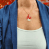 Collana fatta a mano con ciondolo a forma di funghetto rosso a pois bianchi, creata con un mosaico di perline di vetro e mostrata sia indossata su espositore sia in primo piano. Indossato