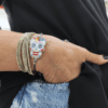 Bracciale con teschio messicano in perline colorate intrecciato su cordino blu in macramè, indossato al polso insieme a bracciali multifilo.