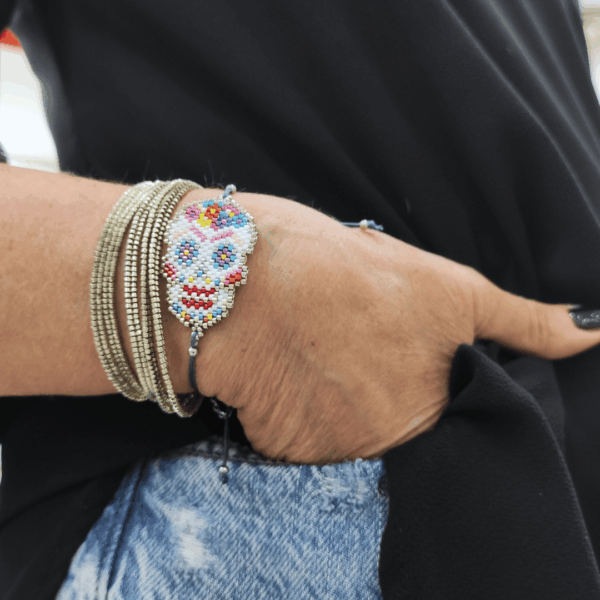Bracciale con teschio messicano in perline colorate intrecciato su cordino blu in macramè, indossato al polso insieme a bracciali multifilo.