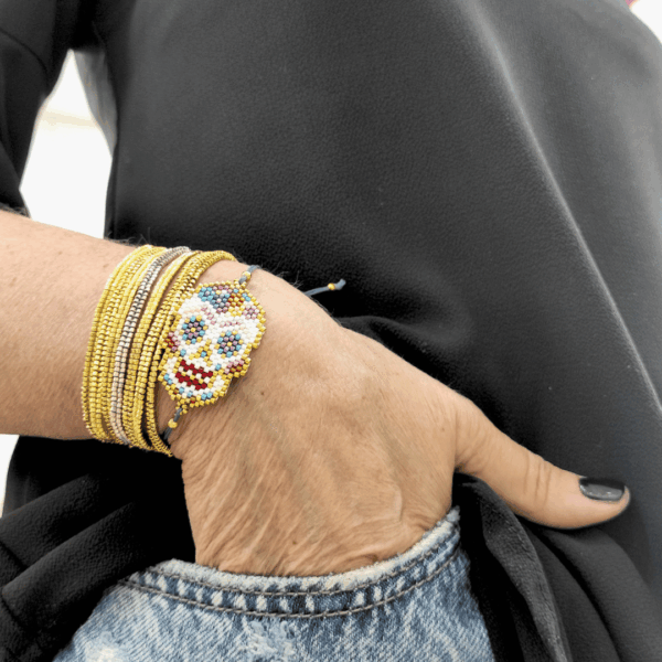 Bracciale con teschio messicano in perline colorate intrecciato su cordino blu in macramè, indossato al polso insieme a bracciali multifilo.