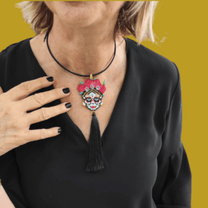 Collana con grande pendente teschio messicano ispirato a Frida Kahlo con fiori rossi in perline e lunga nappa nera in tessuto, indossata su cordino nero rigido.