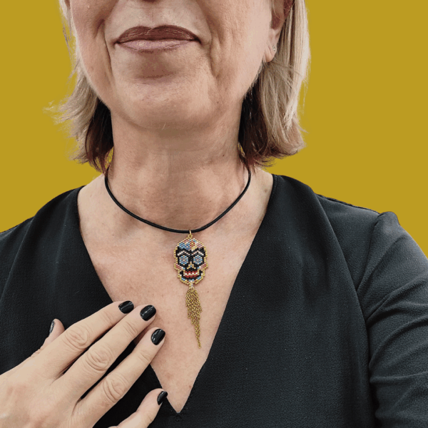 Collana Vanitage con pendente teschio messicano in perline colorate e frange pendenti di catenelle argentate, indossata su cordino rigido nero.