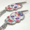 Dettaglio Orecchini pendenti Vanitage con teschio messicano in micro-perline multicolor e lunghe frange di catenelle argentate a movimento fluido, indossati al lobo.