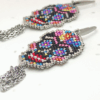 Dettaglio Orecchini pendenti Vanitage con teschio messicano in micro-perline multicolor e lunghe frange di catenelle argentate a movimento fluido, indossati al lobo.