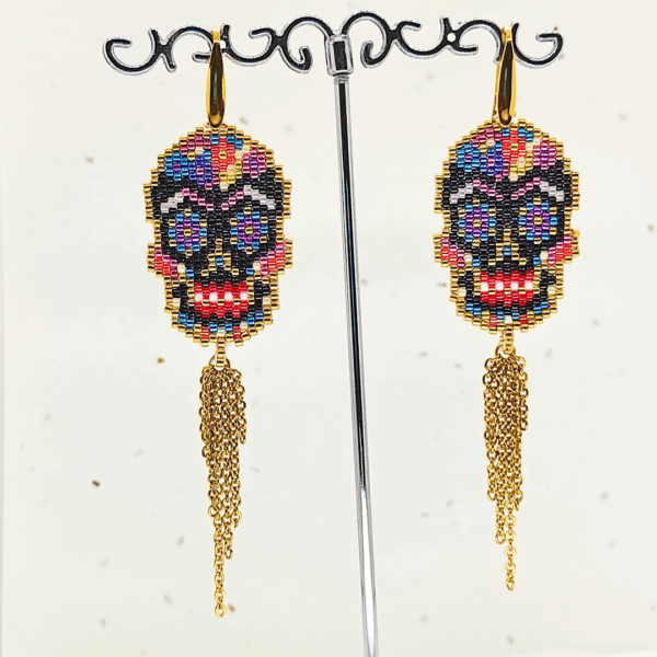 Orecchini pendenti Vanitage con teschio messicano in micro-perline multicolor e lunghe frange di catenelle argentate a movimento fluido, indossati al lobo.