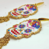 Dettaglio Orecchini pendenti Vanitage con teschio messicano in micro-perline multicolor e lunghe frange di catenelle argentate a movimento fluido, indossati al lobo.