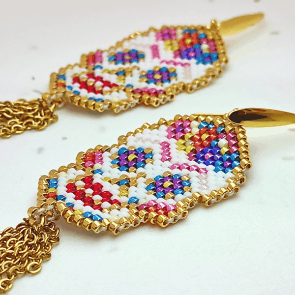 Dettaglio Orecchini pendenti Vanitage con teschio messicano in micro-perline multicolor e lunghe frange di catenelle argentate a movimento fluido, indossati al lobo.